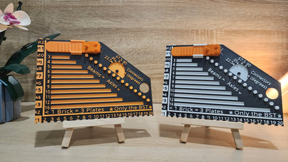 Two brick rulers next to each other. Black and orange on the left and the black and white on the right. There is a Lego flower and Lego pot behind the black and orange ruler on the left.