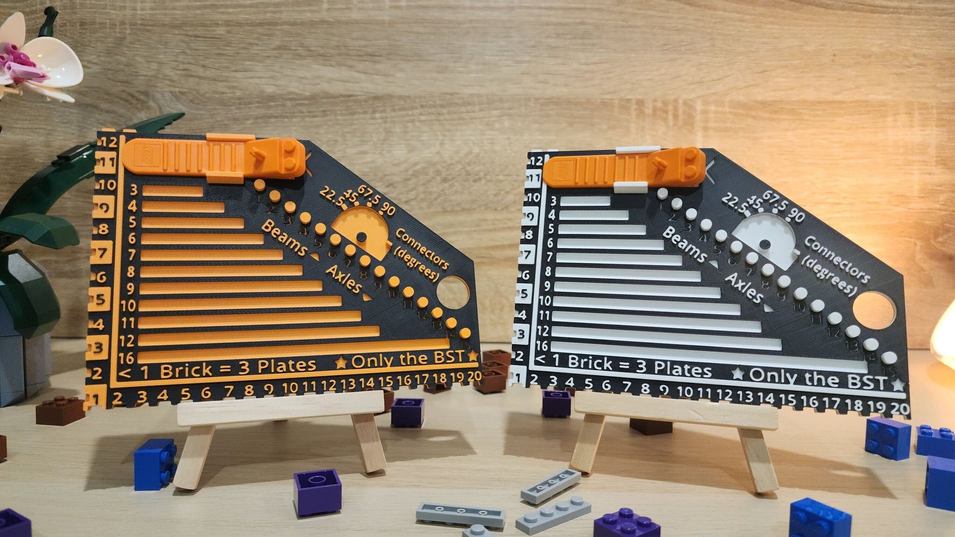 Two brick rulers next to each other. Black and orange on the left and the black and white on the right. There are some Lego pieces arround the brick rulers.