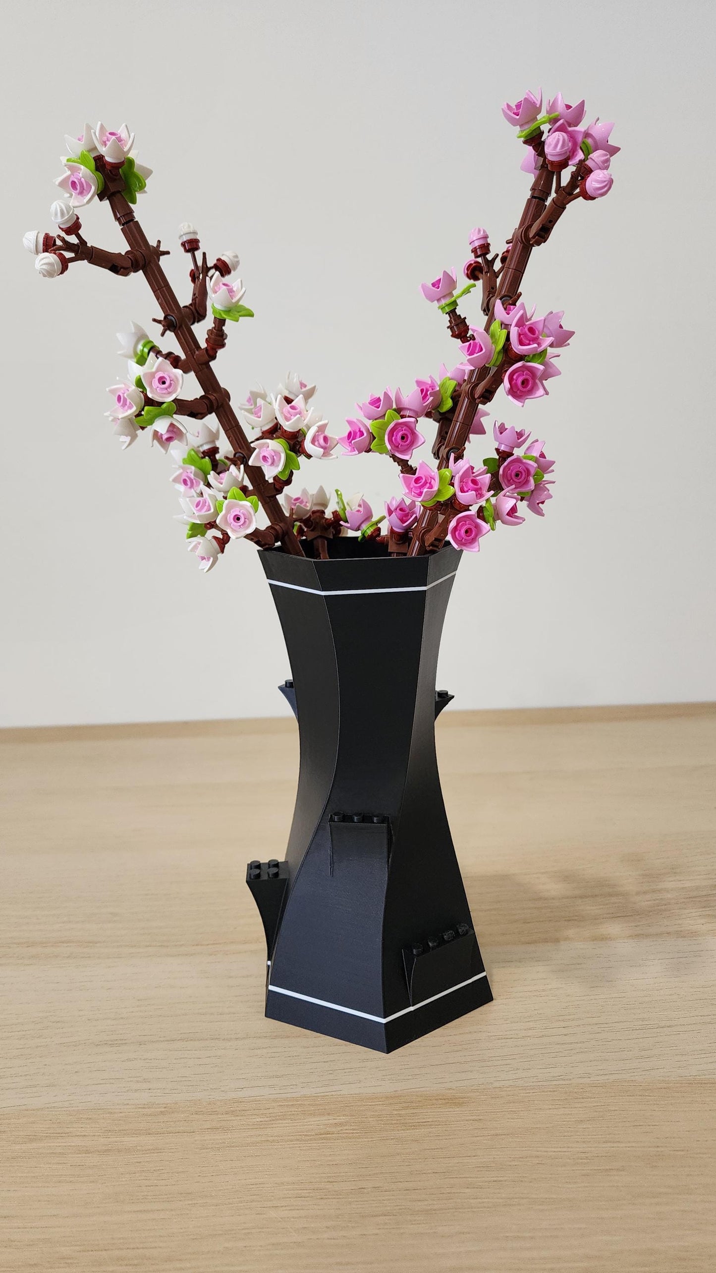 Black and White LEGO-Compatible Vase holding pink LEGO cherry blossom stems on wooden surface